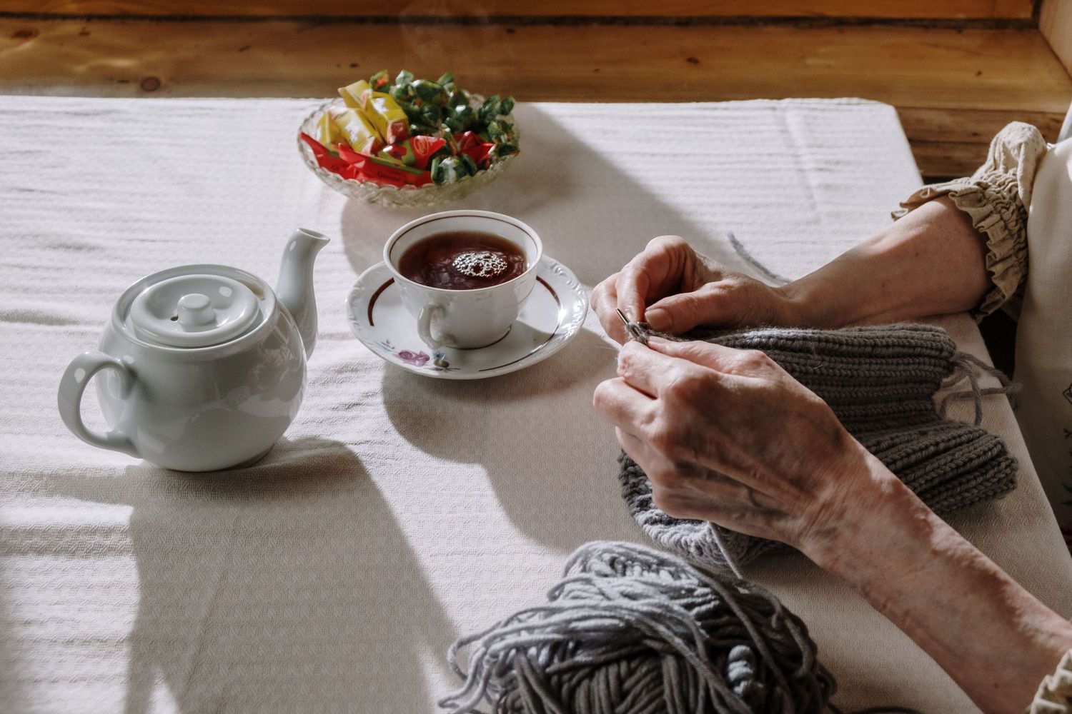 Eine Teekanne und eine Tasse Tee auf dem Tisch, daneben Hände mit Strickzeug.